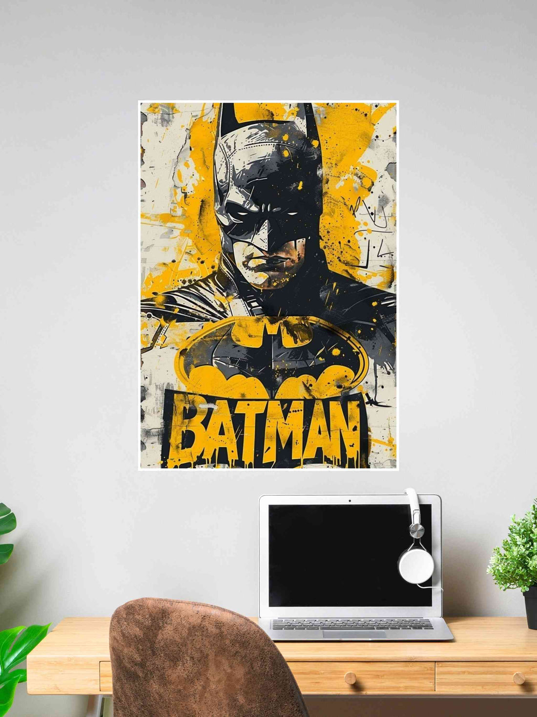Grunge-style Batman poster with bold yellow splashes and graffiti-like text, displayed above a desk with a laptop and headset.